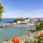 A sunny harbour in Tenby, Wales, filled with small boats and surrounded by colourful buildings near a Christian holiday flat and stone sea walls.