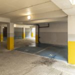 An empty underground car park for a Tenby Christian holiday flat, featuring concrete columns painted yellow at the base and blue-painted parking bays.